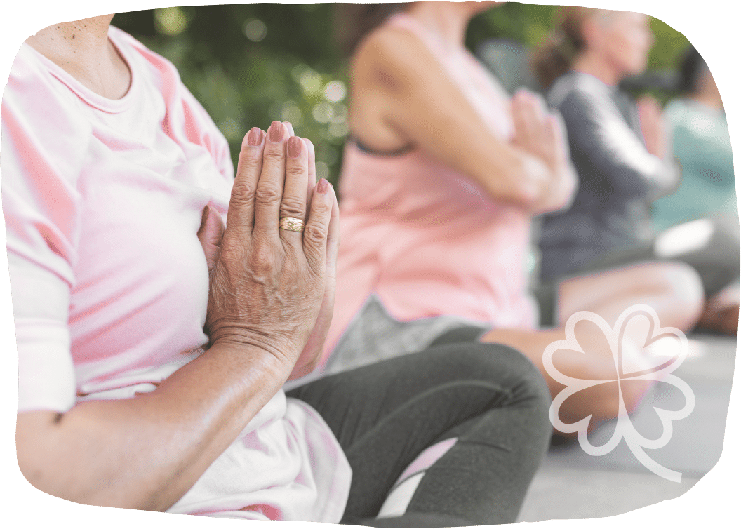 Mehrere Menschen sitzen im Freien im Yogasitz mit gefalteten Händen – Ausdruck von Gemeinschaft, Heilung und innerer Ruhe.