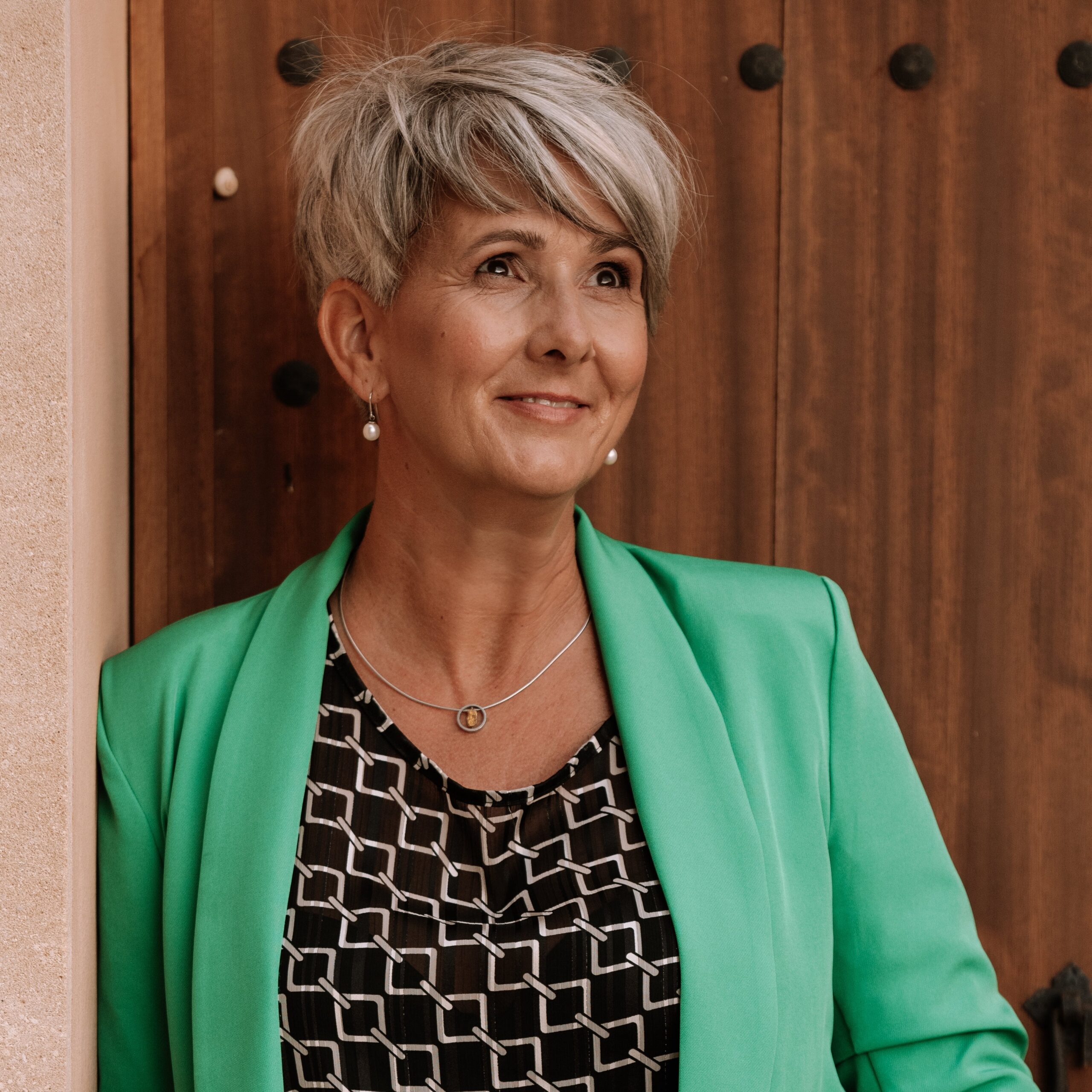 Frau in grünem Blazer vor Holzhintergrund