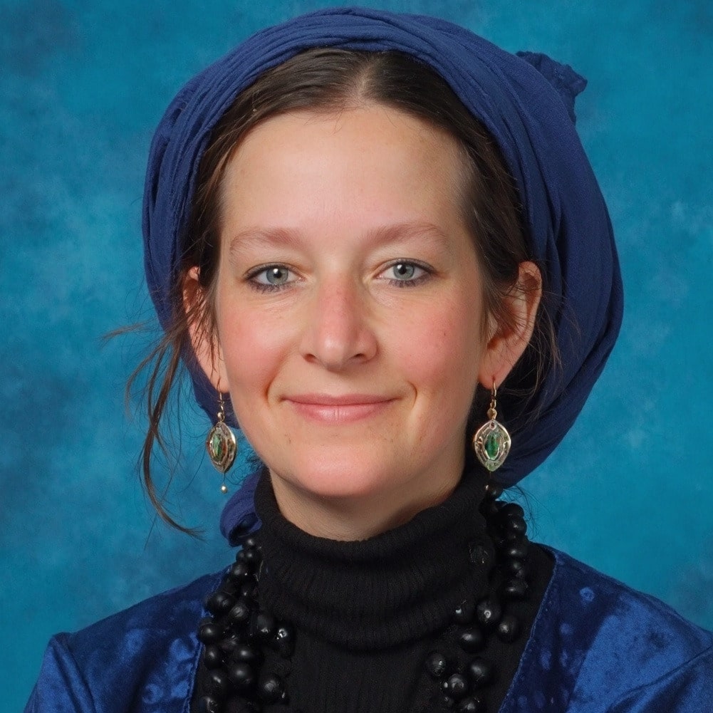 Frau mit blauem Kopftuch und Schmuck lächelt