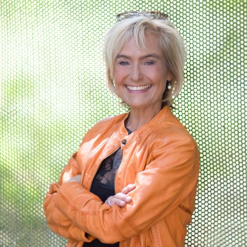 Lächelnde Frau in orangefarbener Jacke im Freien